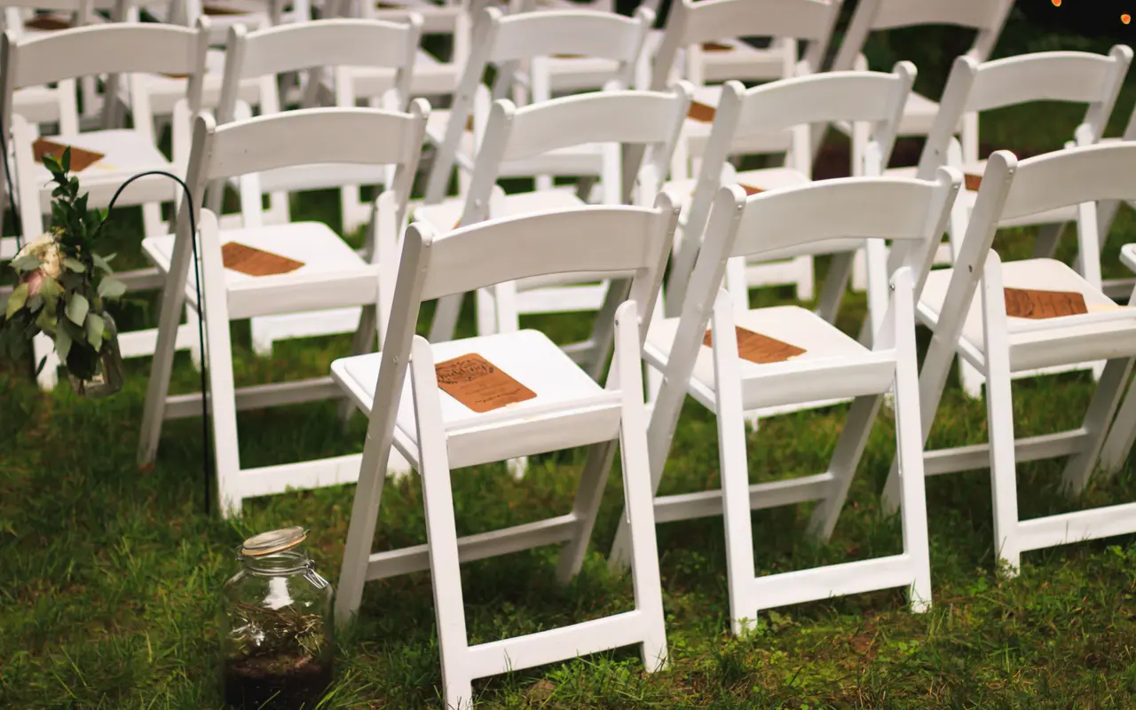 White folding chairs set in rows on grass for an outdoor garden ceremony